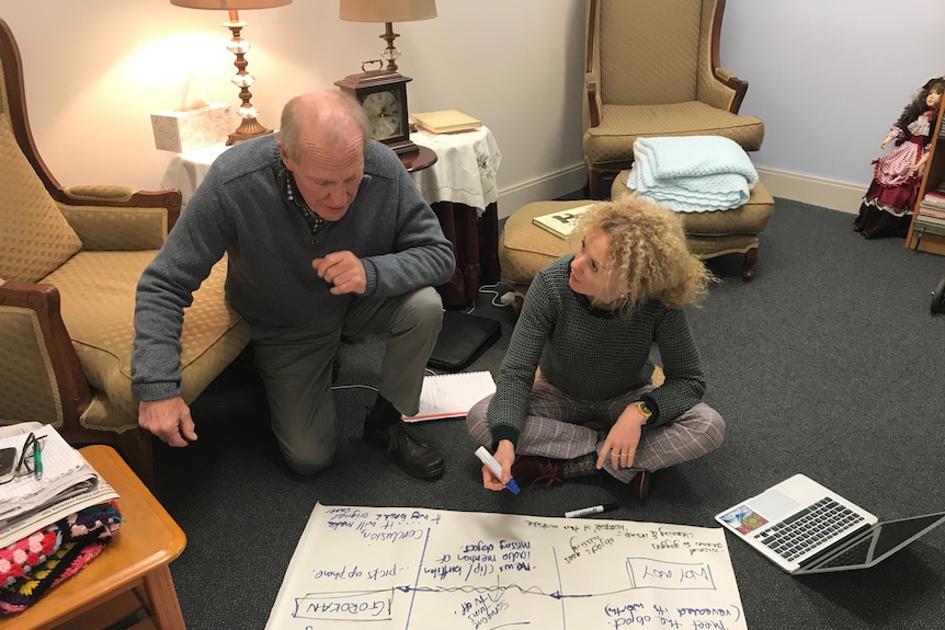 an older man leans over a younger woman and a piece of butcher's paper scribbled with ideas