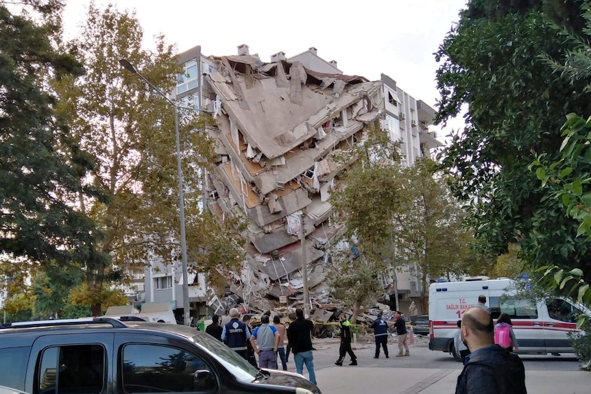 People on the street look at a damaged  building in Izmir, Turkey. One corner of the building has collapsed