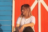 一个女生坐在海滩的一栋小房子前