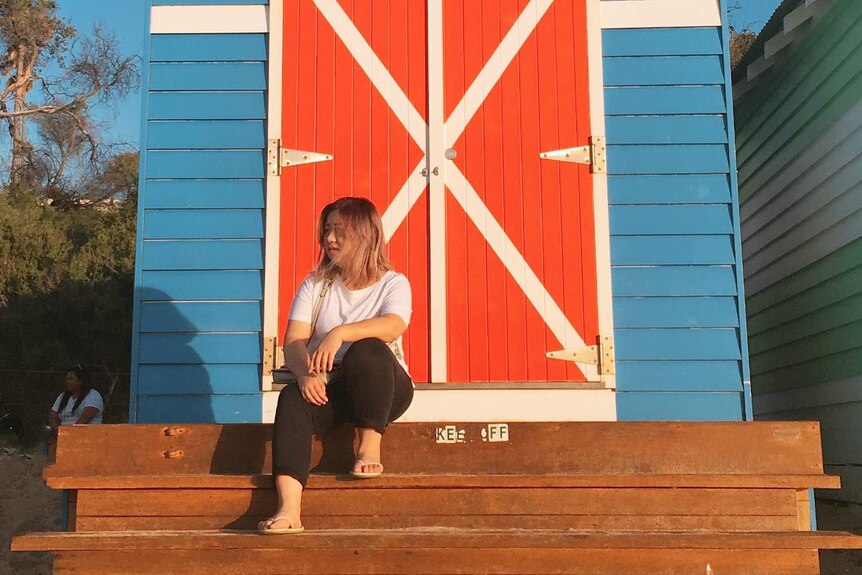 A woman sits in front of a beach box.