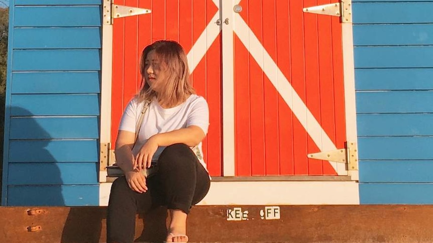 A woman sits in front of a beach box.