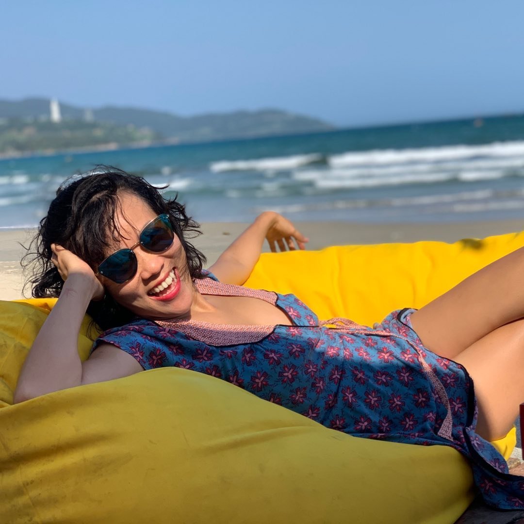 A woman laughs while sitting on a bean bag on a beach in Vietnam