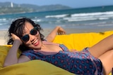 A woman laughs while sitting on a bean bag on a beach in Vietnam