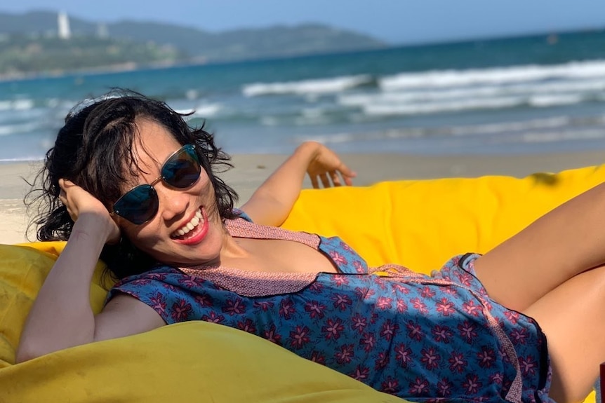 A woman laughs while sitting on a bean bag on a beach in Vietnam