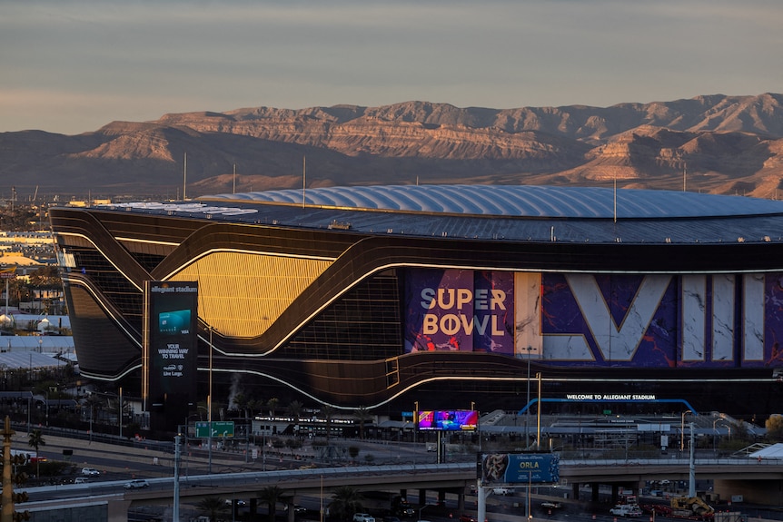 Allegiant Stadium, which has an enclosed roof, in the afternoon sun with rocky mountains behind it
