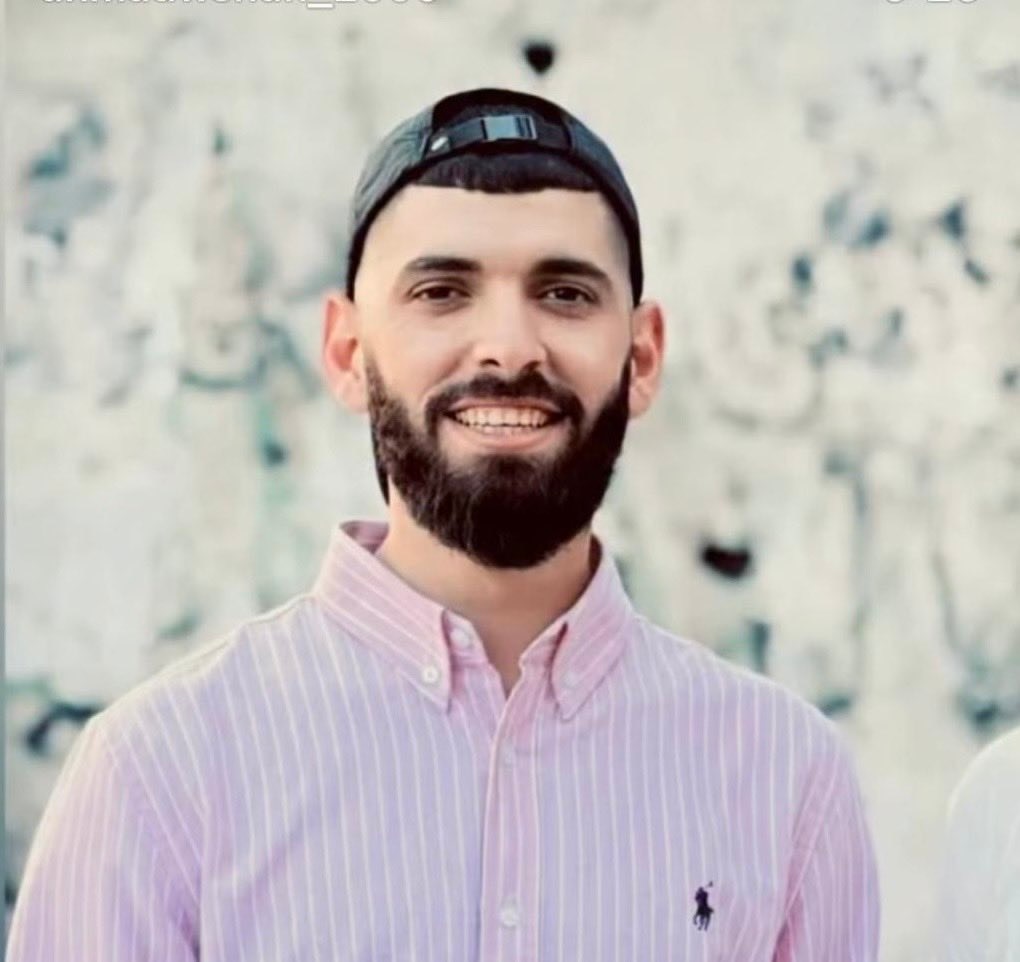 A man wearing a black cap backwards and a pink shirt smiling
