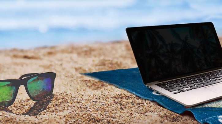 Photo of sunglasses and a laptop on a beach 