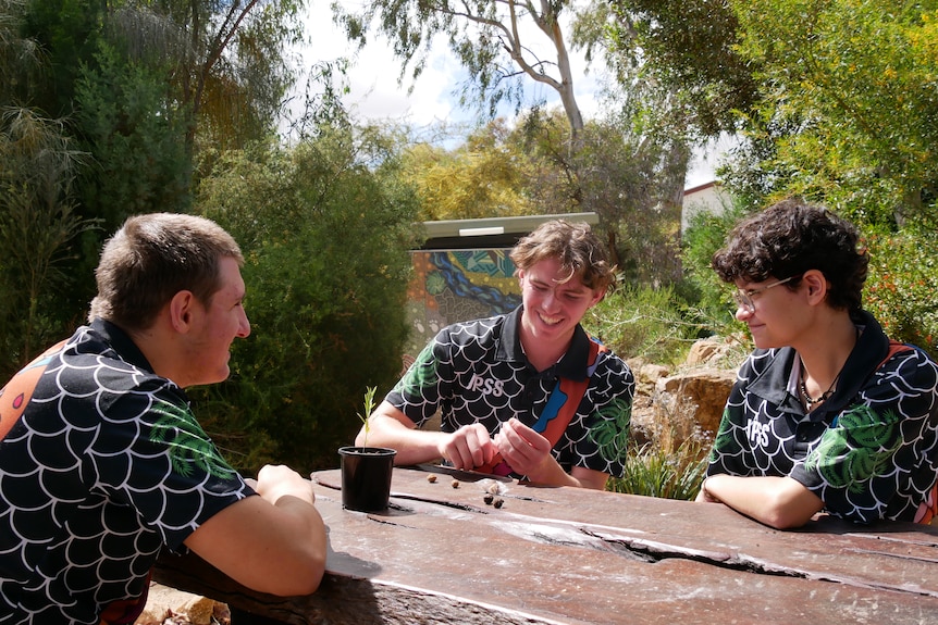 Three high school students sit around an outdoor table.