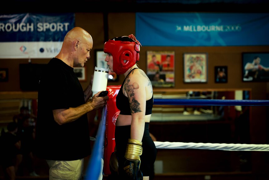 Marissa Williamson-Pohlman at the gym with a coach, wearing a red head protector, talking in the corner
