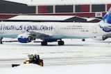 A tractor with a snow plough attached clears snow between parked aircraft at Manchester Airport