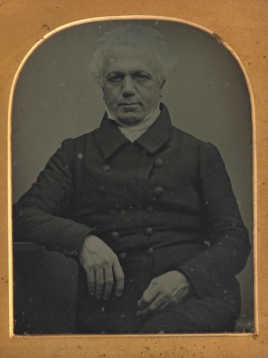 A black and white photo of a man in a gold and red frame. 