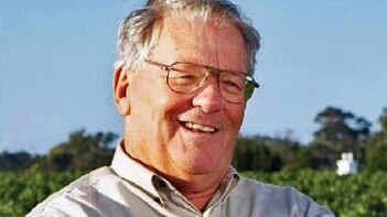 A head and shoulders shot of Michael Wright smiling outdoors in a vineyard wearing spectacles and a grey shirt under a blue sky.