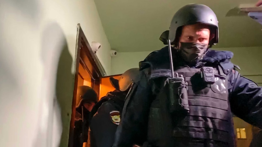 Police stare forward as they leave the apartment where Oleg Navalny lives wearing helmets and flack jackets.