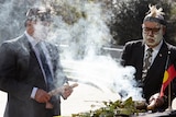 Two men participate in a traditional Aboriginal smoking ceremony.