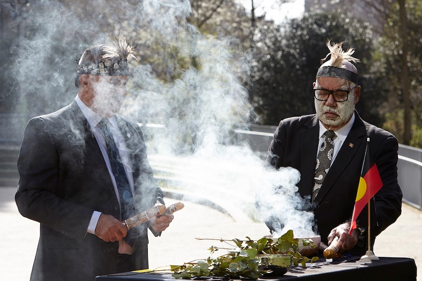 Two men participate in a traditional Aboriginal smoking ceremony.