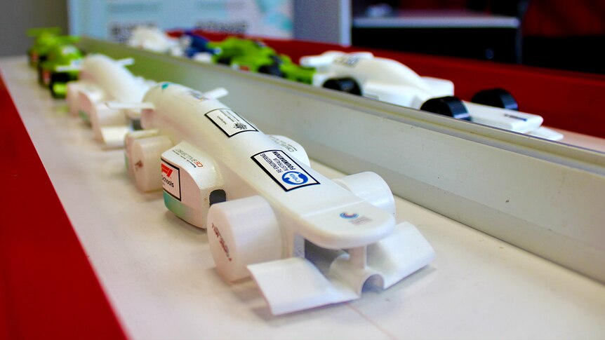 Eight compressed gas cylinder powered race car models lined up for display on a track.