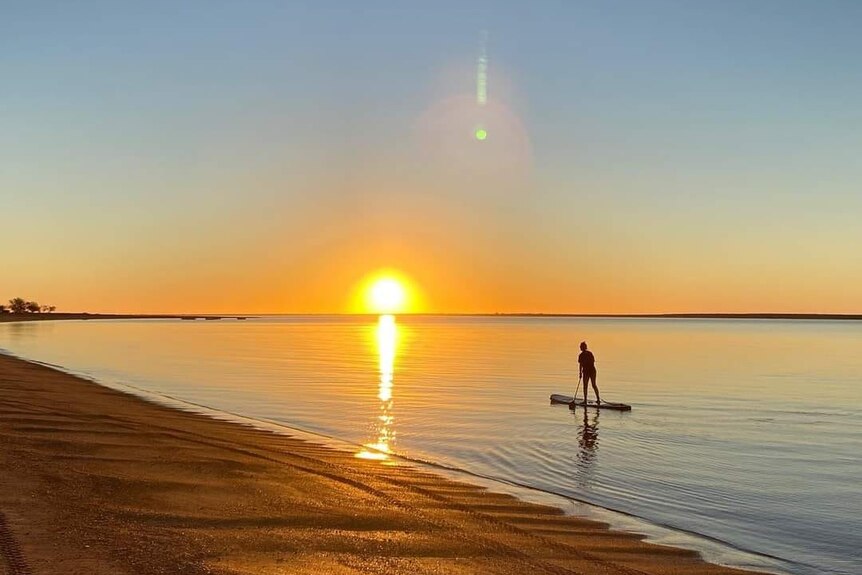 A lone paddle boarder with a sunset