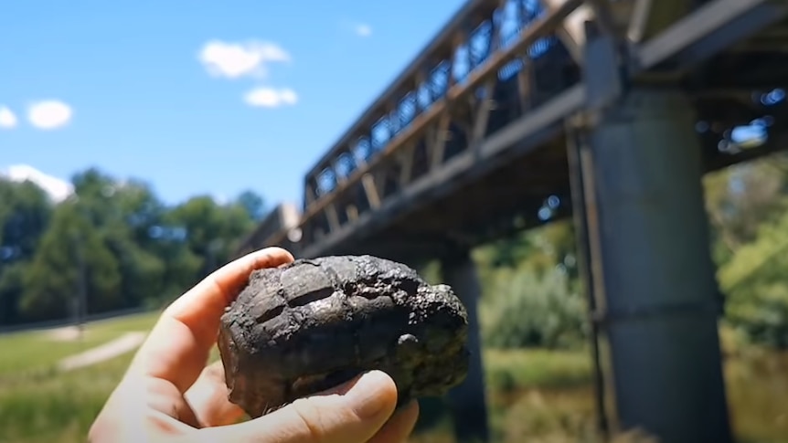 A hand holding a metal grenade in front of a bridge.