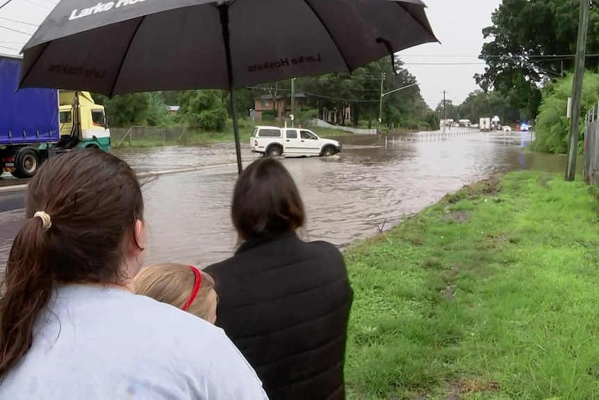 people watch rising water on road holding an unbrella