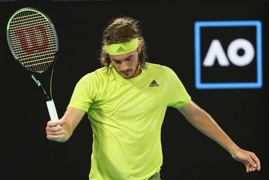 A headband-wearing tennis player looks down as he brandishes his racquet after losing a point.