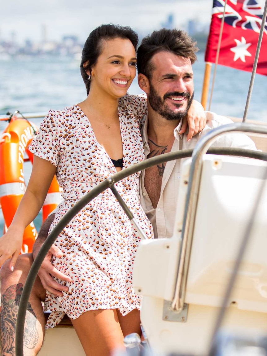 A man and a woman embrace while he drives a boat on the water