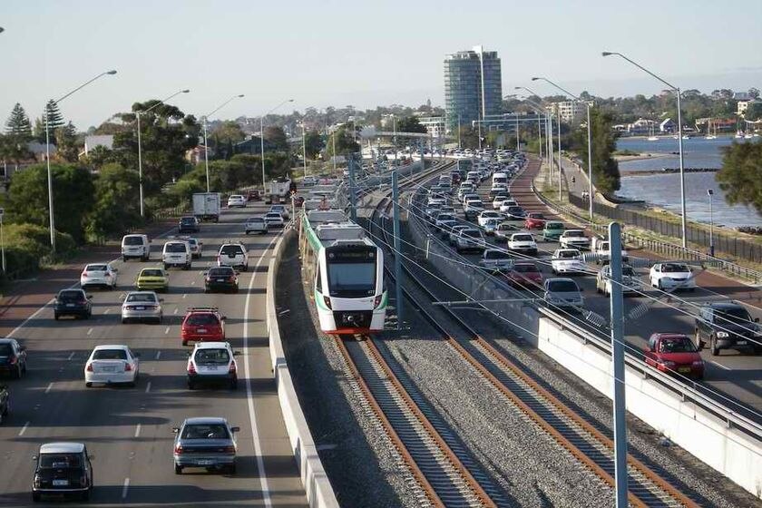 A train runs on the Perth to Mandurah rail line with cars either side on the freeway.