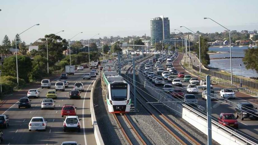 A train runs on the Perth to Mandurah rail line with cars either side on the freeway.