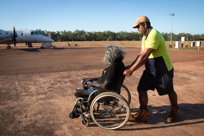 A man being pushed in a wheelchair towards a small plane.