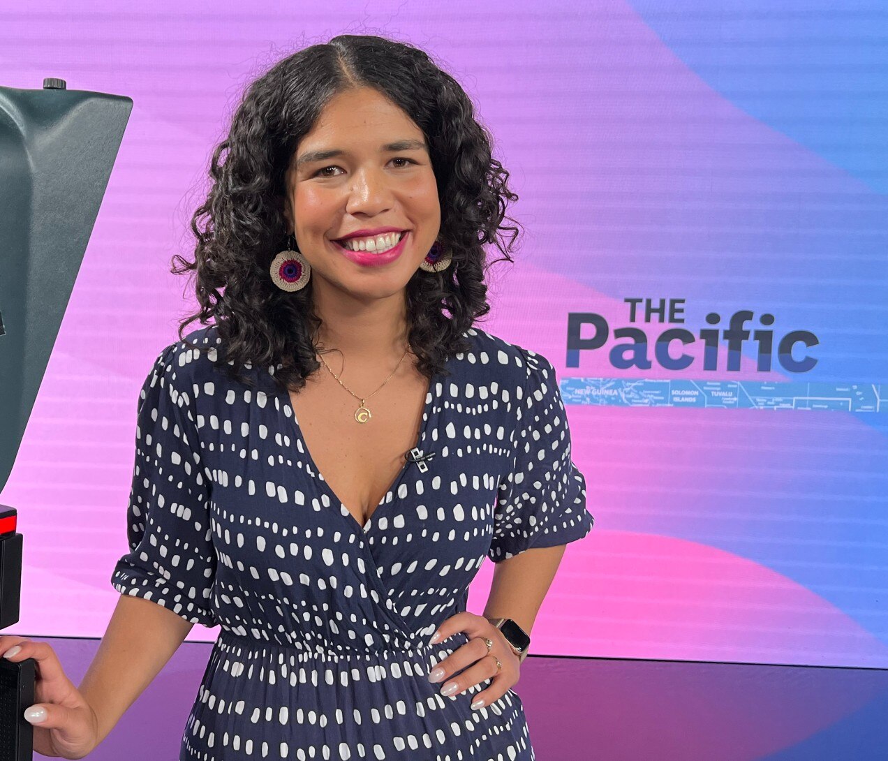 Woman leaning on camera in TV studio with backdrop saying The Pacific.