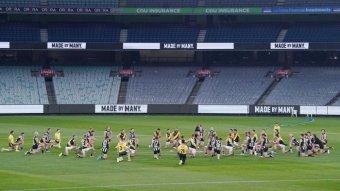Players from two AFL teams go on one knee in the centre circle ahead of their match at the MCG.