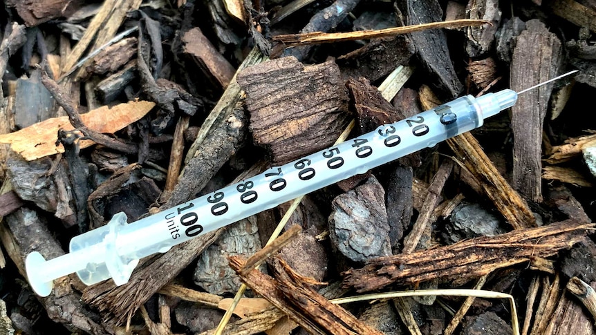 A discarded syringe in a pile of woodchips.