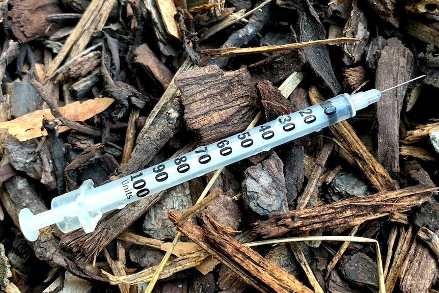 A discarded syringe in a pile of woodchips.