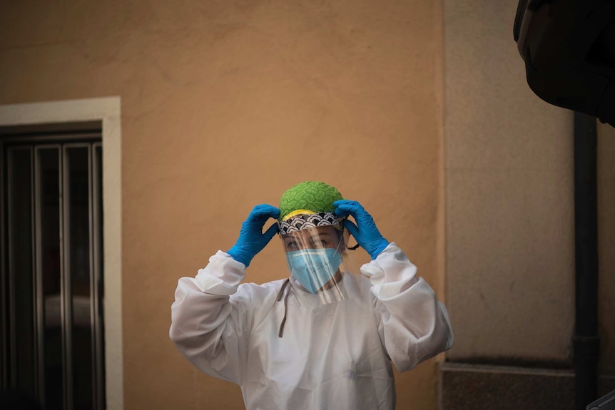 A doctor fixes a protective mask to her face with gloved hands