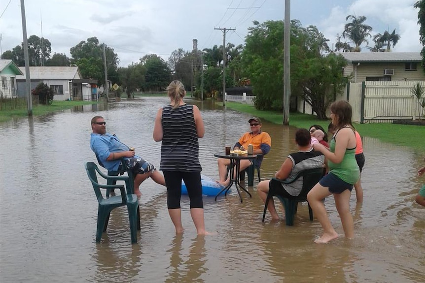 A group of residents sit in chairs in floodwaters at Giru