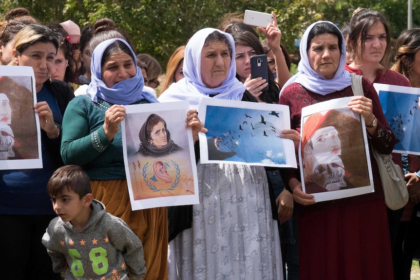 A group of women holding pictures, standing at a vigil.