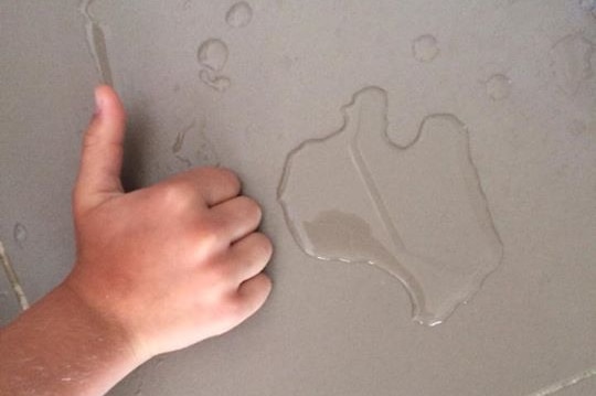 A puddle shaped like a map of Australia with a person giving the thumbs up sign beside it