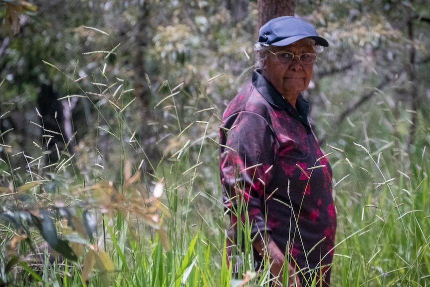 Older Aboriginal woman standing amongst grass and scrubland
