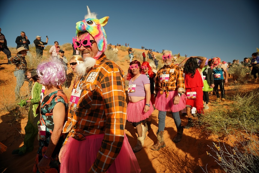 A group of people in bright costumes surrounded by red dunes.