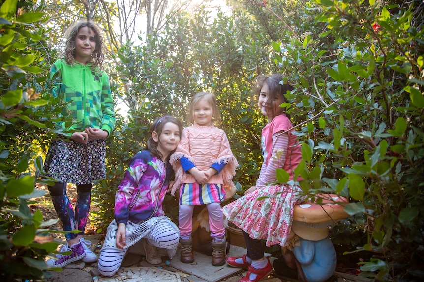 Four young girls sit in a garden with fairy and mushroom statues.