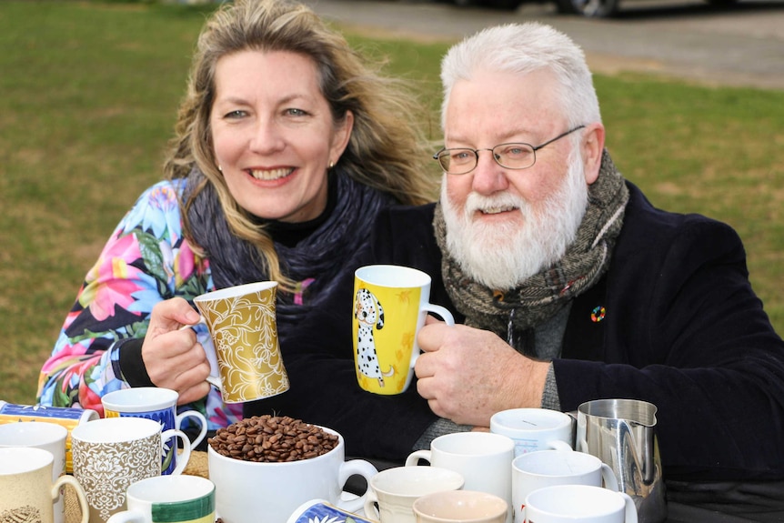 Salamanca Market stallholder Izabella Williamson and Hobart councillor Bill Harvey crouch down holding mugs