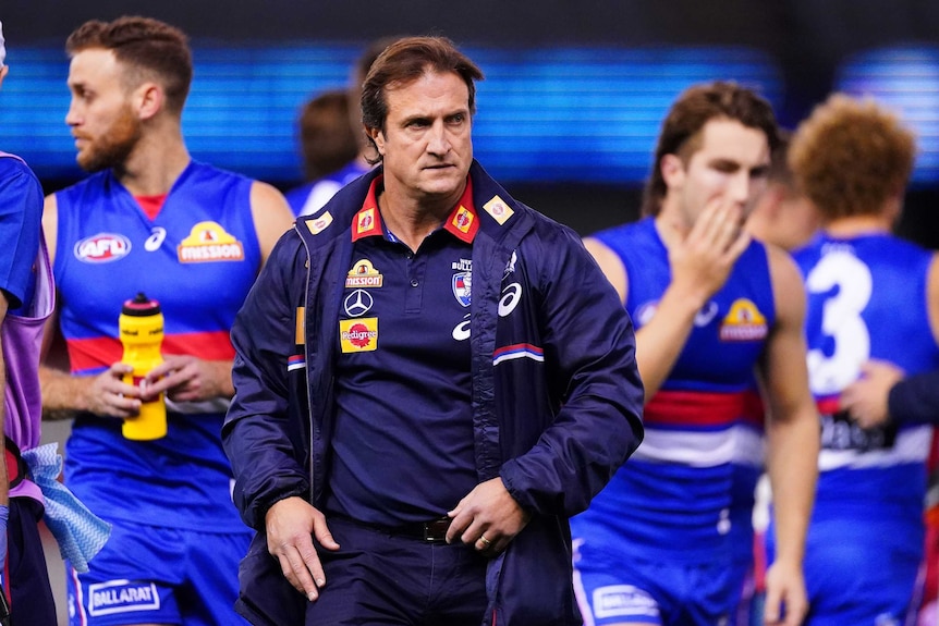 The Western Bulldogs AFL coach leaves the field after a quarter-time address with his players in the background.