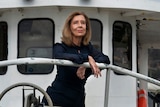 Kathyryn Heyman with shoulder length brown hair stands at end of a boat looking out over water.