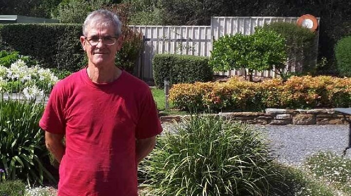 man in a red top and glasses standing in front of backyard garden