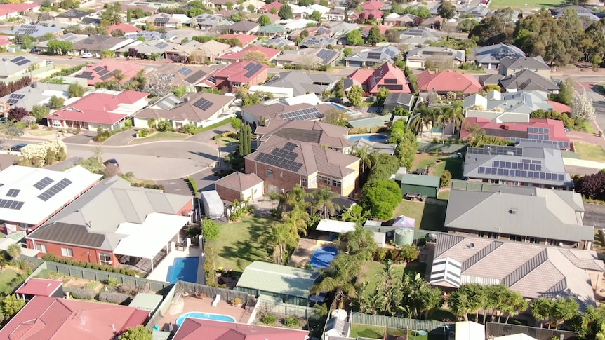 Drone shot of houses, some with solar panels on their roofs and backyard pools