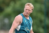 A male rugby union player, in a green training singlet, looks over his right shoulder and grimaces