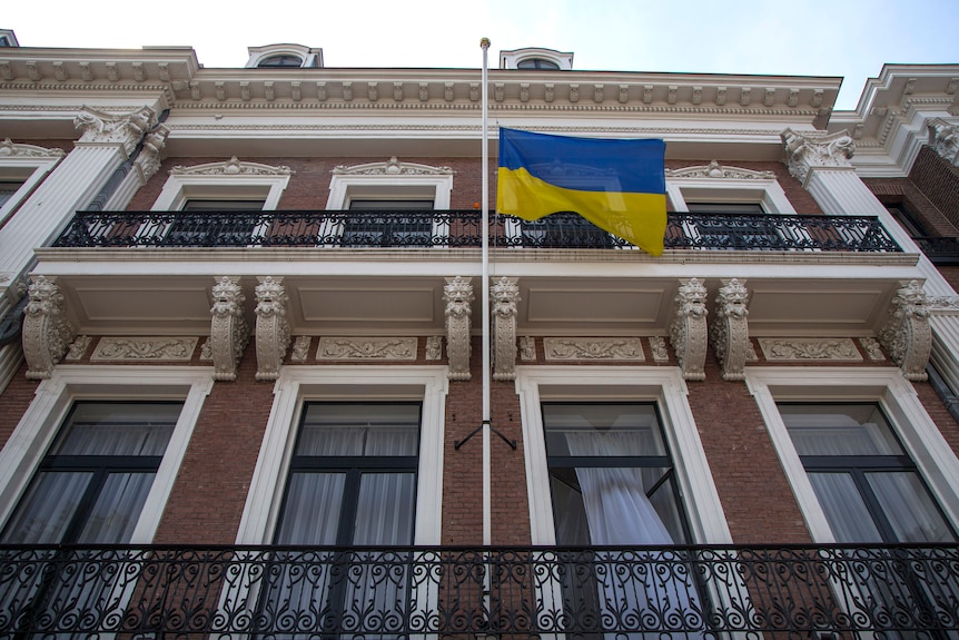 The front of a large old building in pictured. A Ukrainian flag is hanging half-staff.