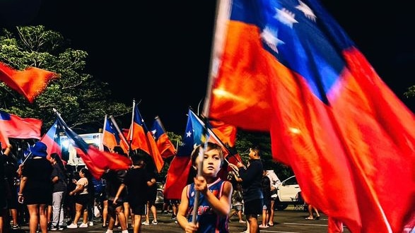Small boy holds large Samoan flag. 