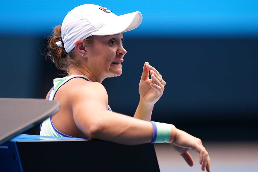 Ash Barty pulls a face and looks over her shoulder whilst sitting at the Australian Open