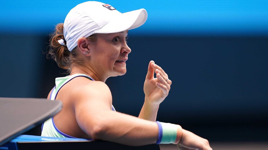 Ash Barty pulls a face and looks over her shoulder whilst sitting at the Australian Open