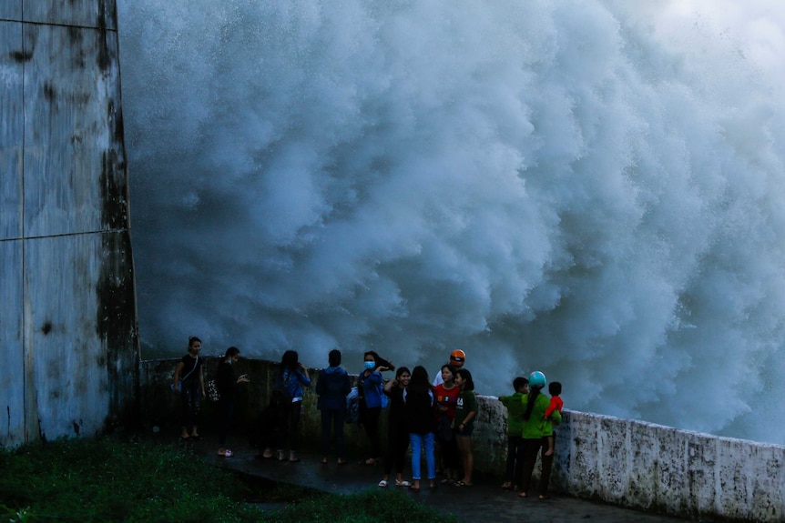 A number of people are standing next to a dam with a burst of water coming out of the flood gates.